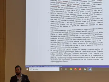 Mężczyzna przy mównicy prezentuje dokument na ekranie w sali konferencyjnej.