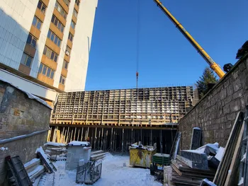 Plac budowy z dźwigiem, rusztowaniami i materiałami budowlanymi obok wysokiego budynku.