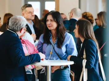 Grupa osób rozmawia przy okrągłym stoliku na konferencji, w tle inni uczestnicy.